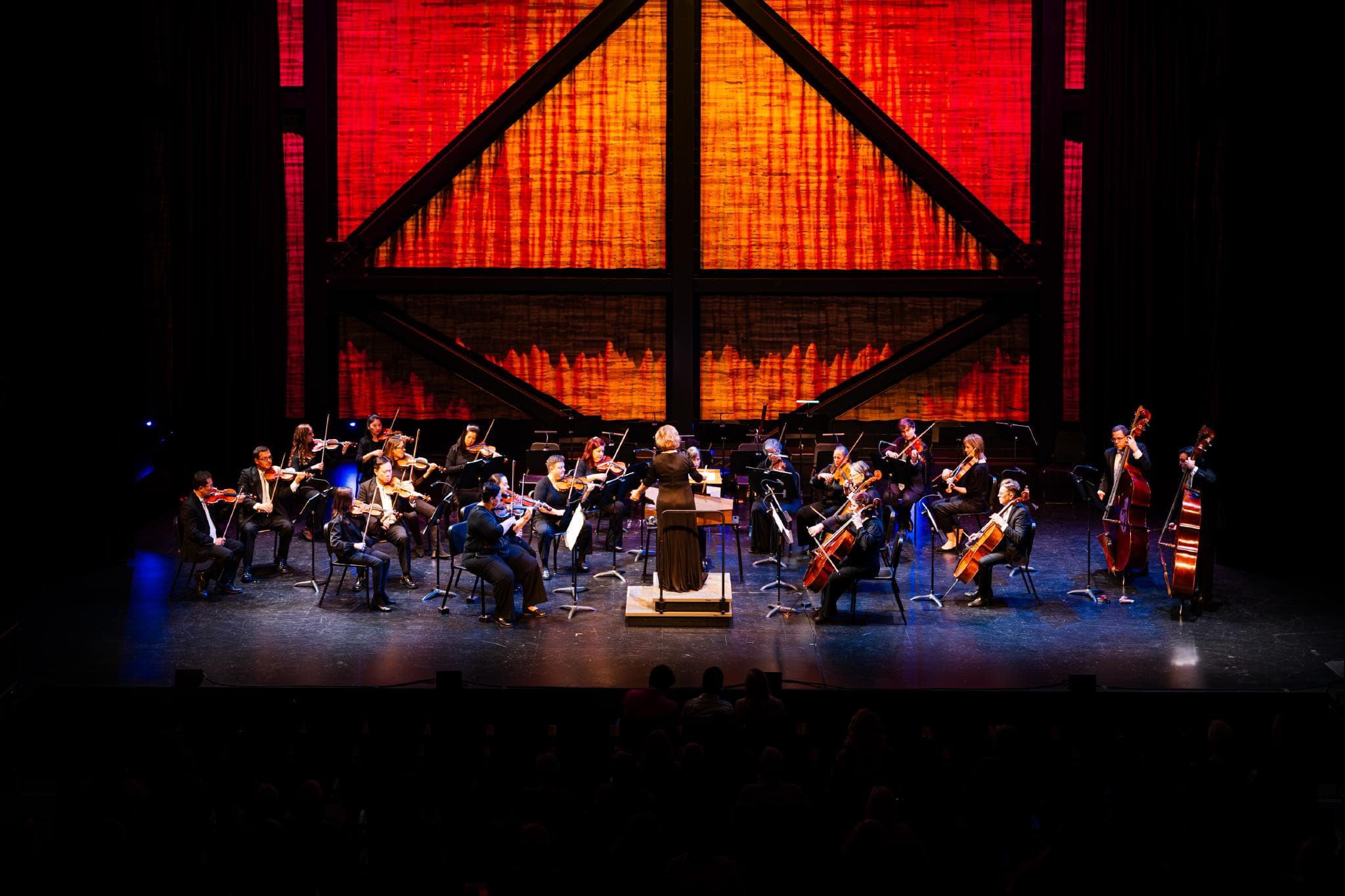 Memphis Symphony Orchestra performing on stage, with a stunning large framed, orange backdrop.