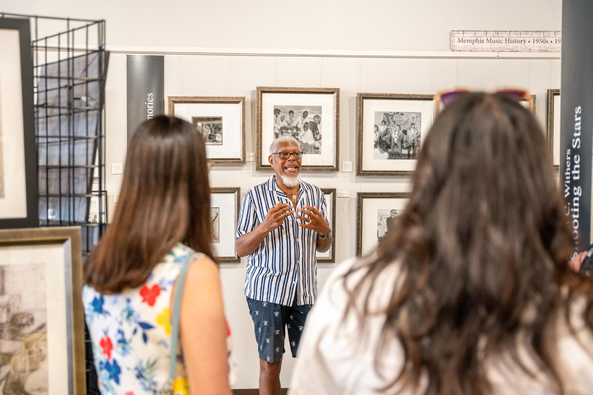 A tour guide leading a group through the Withers Collection Museum & Gallery, with photos behind him.
